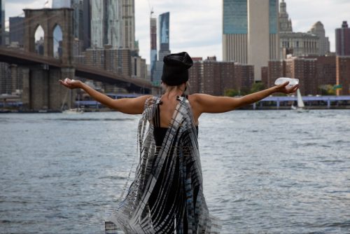 A person standing in front of a body of water with the arms out Description automatically generated with medium confidence