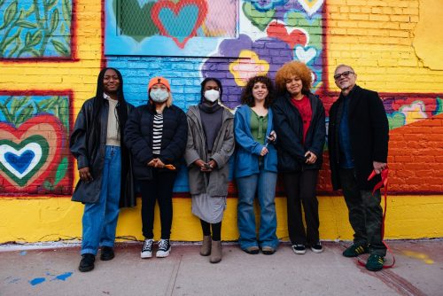 A group of people standing in front of a wall with graffiti Description automatically generated