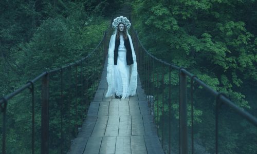 A person in a white dress and headdress on a bridge Description automatically generated with low confidence