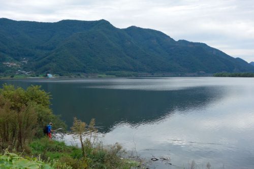 A person standing next to a body of water with a mountain in the background Description automatically generated with medium confidence