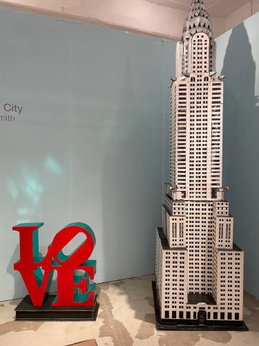 A model of a building next to a red sign Description automatically generated with low confidence