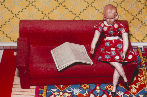 A doll sitting on a couch with a book Description automatically generated with medium confidence