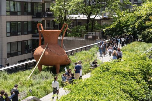 A group of people walking on a path near a large pot Description automatically generated
