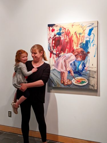 A person holding a child in front of a painting Description automatically generated
