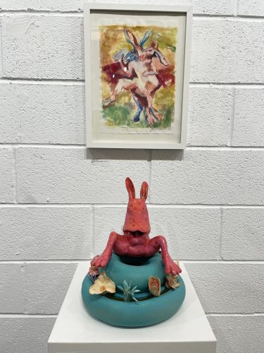 A red crab statue on a white surface next to a painting Description automatically generated