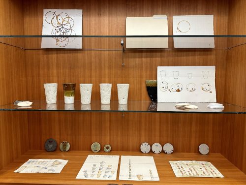 A glass shelves with papers and cups on it Description automatically generated