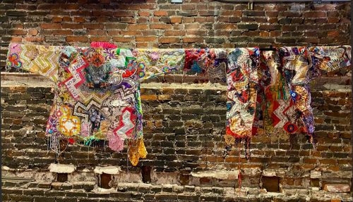 A group of colorful blankets on a brick wall Description automatically generated